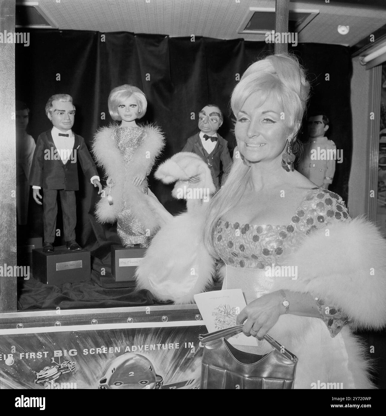 Co-creator of the popular marionette  television series Sylvia Anderson is seen with Lady Penelope (background), when Sylvia attended the world  premiere  of the film Thunderbirds Are Go at the London  Pavilion .  Other members of the International  Rescue  Tracy family seen here are ex-astronaut millionaire  father of the five who form International Rescue  Jeff Tracy ( left) and the chauffeur Parker (holding a garment ) .  As well as being Lady Penelope's  voice ,  Sylvia produced the film . All the marionettes were guests of honour at the premiere .    12 December 1966 Stock Photo