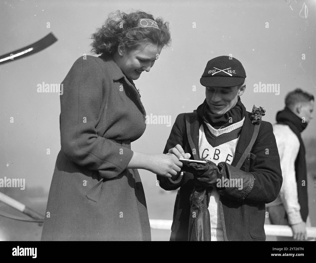 Easter holiday crowds lined the Putney to Mortlake course today, (Saturday), to witness London's greatest show, the 94th inter-Varsity boat race between Oxford and Cambridge. Picture shows: 'sign please' Miss Rosamond Calder of Putney, captures the autograph of Oxford's cox R.G.B Faulker, before he takes the crew for a last outing before the race today (Saturday).    27th March 1948 Stock Photo