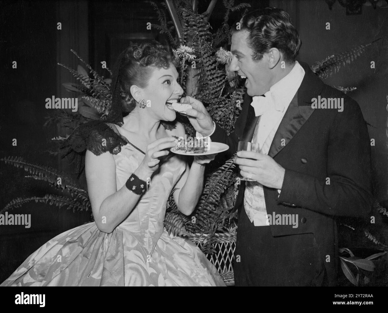 Mary Martin takes a bite of cake offered to her by Graham Payn during a time honoured function which was revived at Theatre Royal, Drury Lane Function. The ceremony dates from 1794 when Robert Baddeley, a pastry cook who became a noted Drury Lane actor, set up a fund for the provision annualy of a cake to be cut in the presence and eaten by his Majesty's company of comedians then appearing as Drury Lane. 6 January 1946 Stock Photo