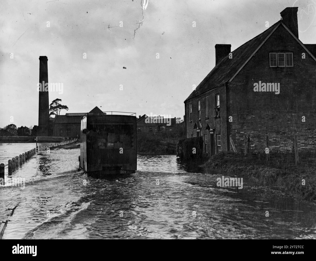 Following torrential rain, accompanied by 40 mph gale, serious flooding in the Stour Valley, Dorset, started yesterday and today the floodwater extended down the valley to Longham, Throop and Iford.  Picture shows cut off from their living rooms, cottages at Longham look out from their bedrooms to watch cars forging through the flooded street.  25 November 1946 Stock Photo