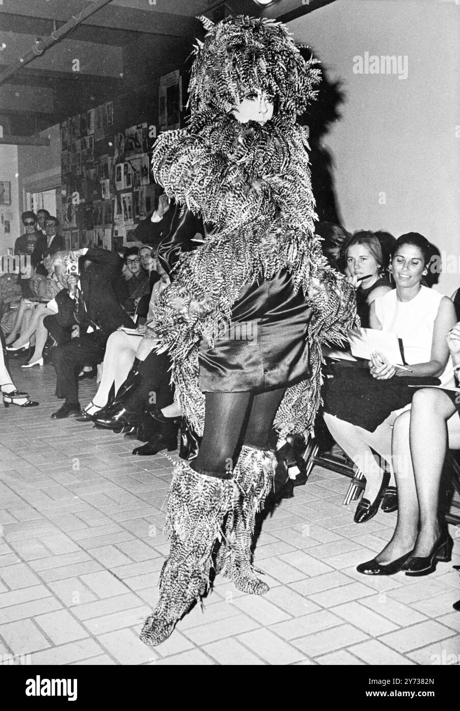 Feathers smother the model as she displays this latest fashion created by Rudi Gernreich during a recent showing in New York .  A short, short dress is the base for a feather  hat , collar , extra long boa and knee-high boots . 12 June 1968 Stock Photo