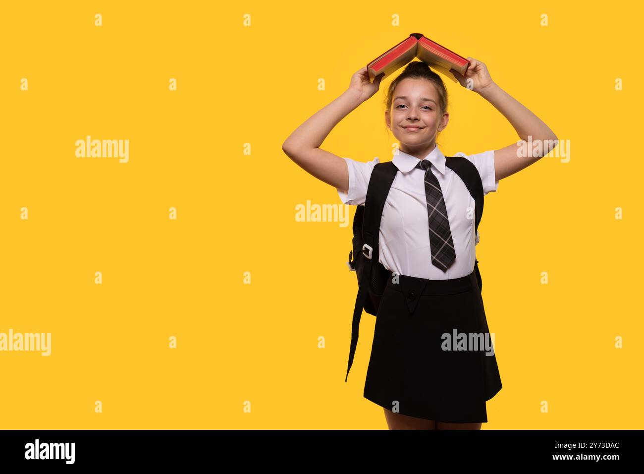 A schoolgirl wearing a uniform holds a book over her head Stock Photo ...