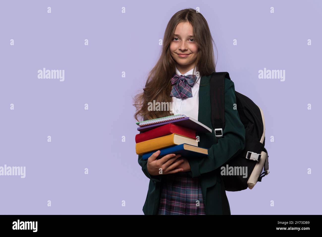 A smiling schoolgirl holds a stack of books while posing confidently ...