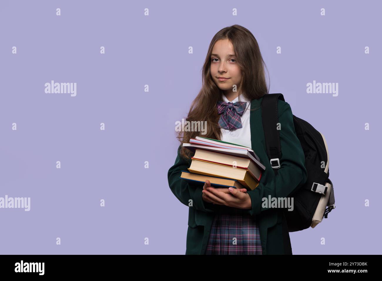 A schoolgirl holding a stack of books while posing with a serious ...