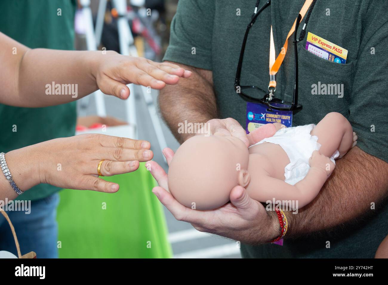 A volunteer shows an attendee how to perform baby CPR at a Health Fair Stock Photo