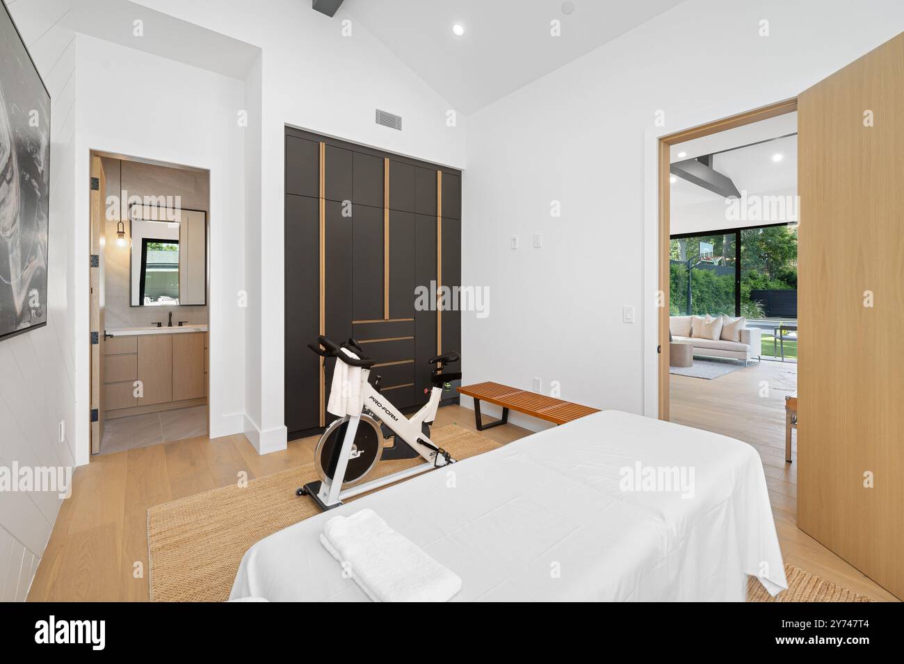 Modern home gym with exercise bike, massage table, and bathroom, featuring sleek design and natural lighting. Stock Photo