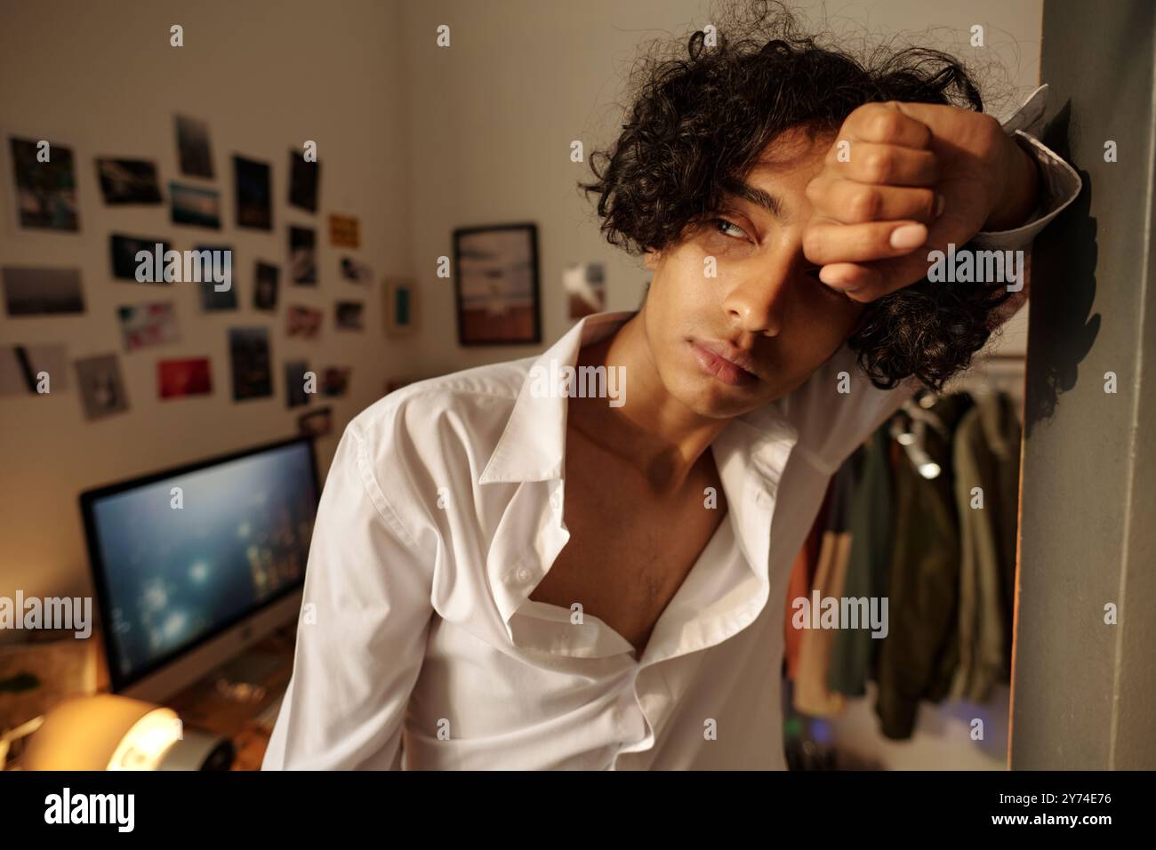 Sick guy in white shirt looking aside through window while standing against wall and suffering from hangover Stock Photo