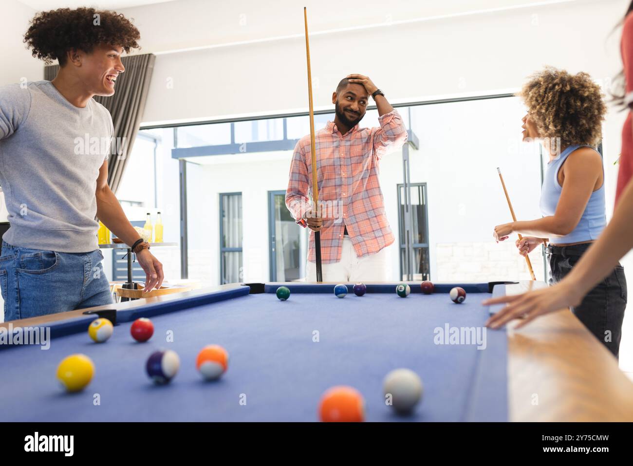 Playing pool, diverse friends enjoying fun hangout together, smiling and laughing, at home Stock Photo