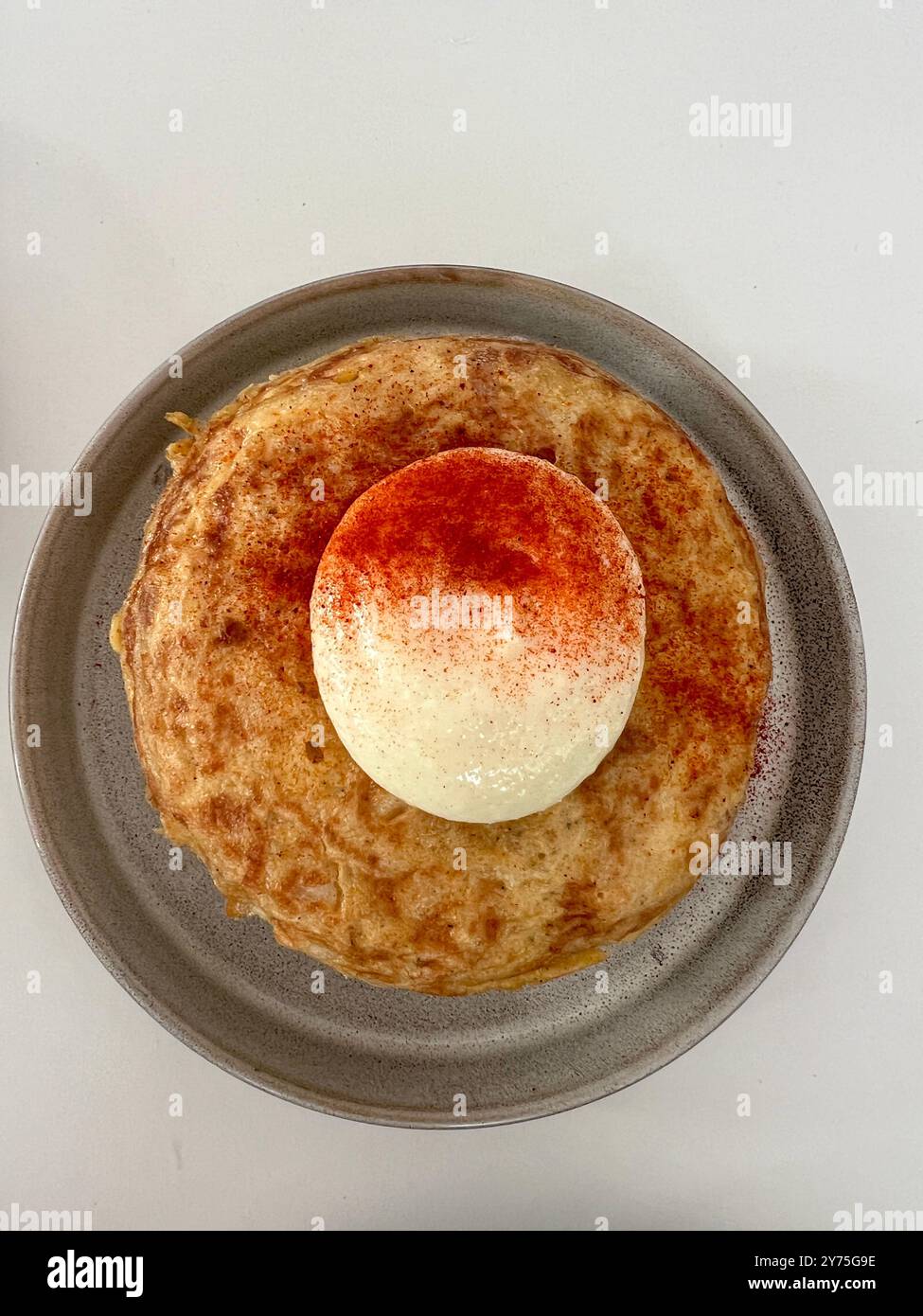 Spanish frittata, common dish in Spain made with eggs and potatoes.  Mayonnaise and paprika topping.  Served on a plate, then on a white background. Stock Photo