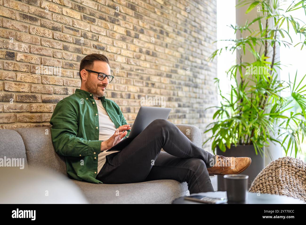 Handsome confident developer working on software over laptop while sitting on sofa in modern office Stock Photo
