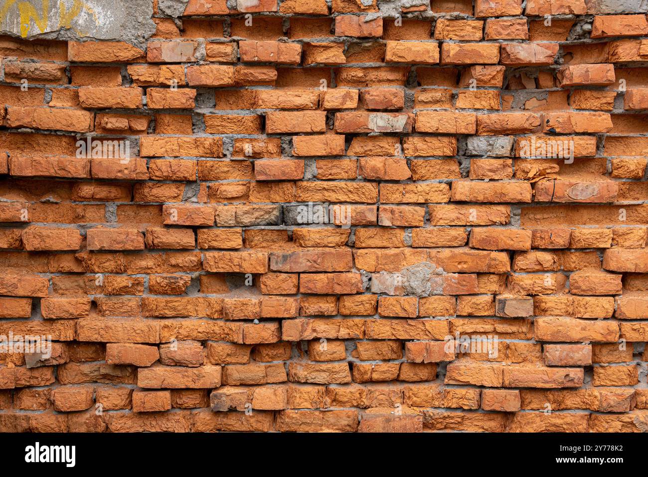 A red brick wall with a few missing bricks. The wall is old and has a rough texture. Stock Photo