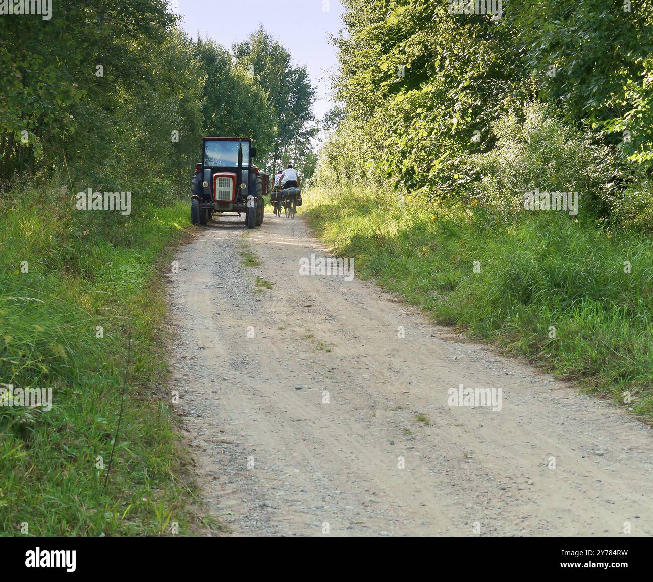 A tractor ride on a gravel road towards cyclists, tourists, tractor in ...