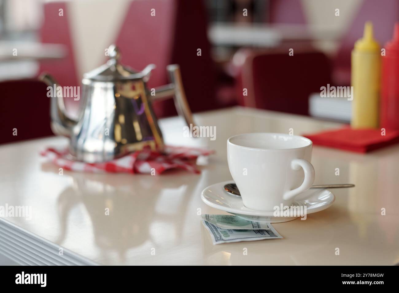 Shiny teapot and white cup on table with condiments in background capturing casual dining ambience in restaurant setting Stock Photo