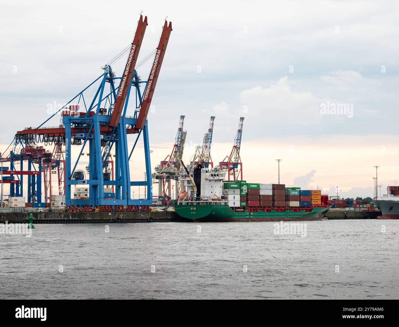Hamburg container terminal with a cargo ship and freight in the docks waiting. The Burchardkai cranes are folded up. Logistics machinery in the harbor Stock Photo