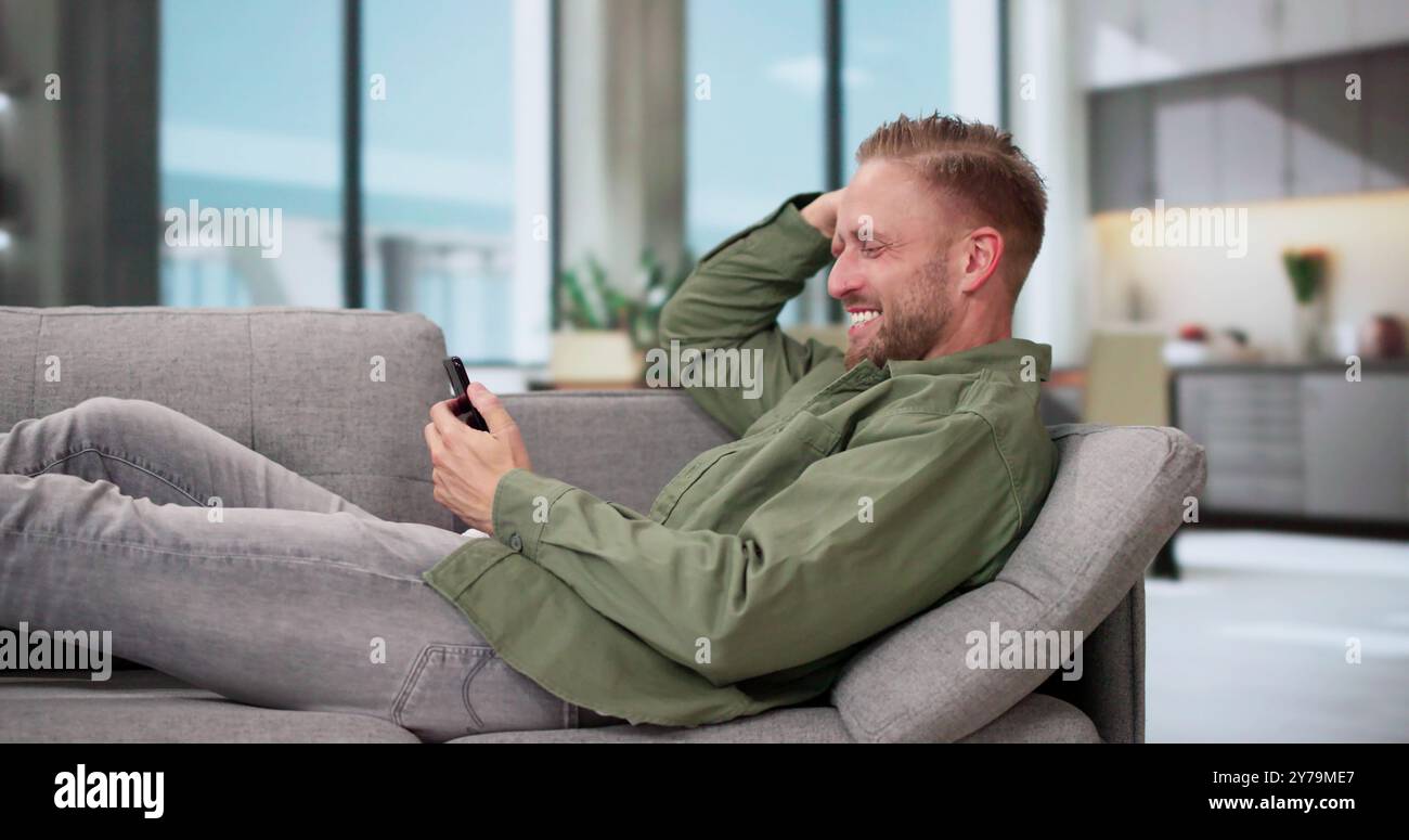Young Happy Man Using Mobile Phone Lying On Sofa Stock Photo