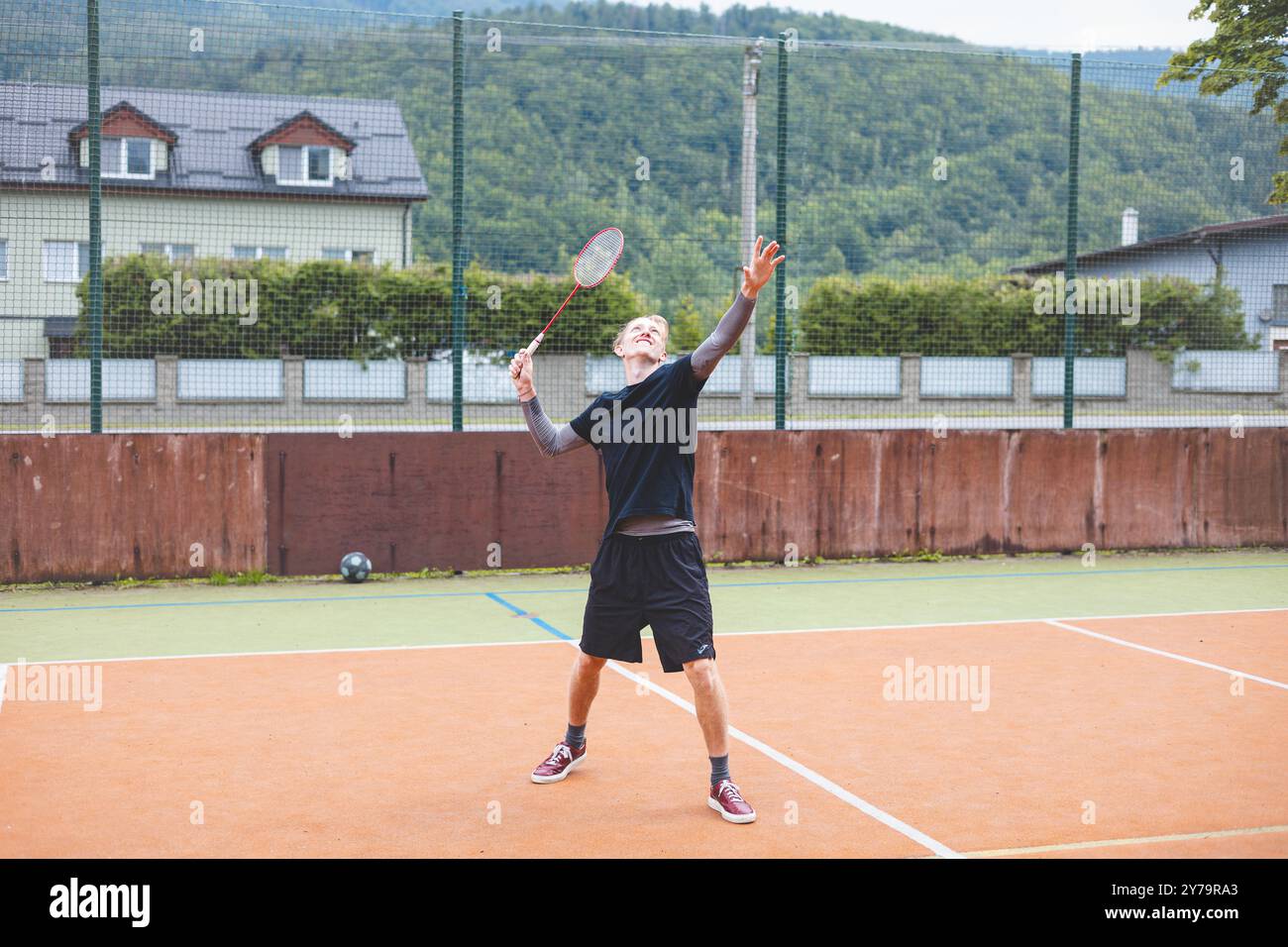 Badminton player stands ready to serve on an outdoor court, holding a ...