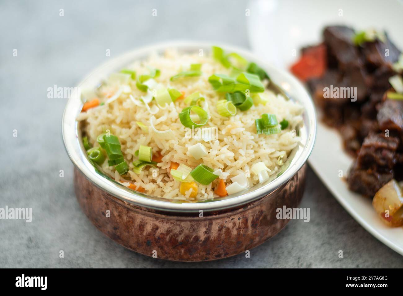 Smoky white rice. Prepared and served in a brass bowl. Natural wood in the background. Fried Rice in a Bowl with Side Dish on black Background. copysp Stock Photo