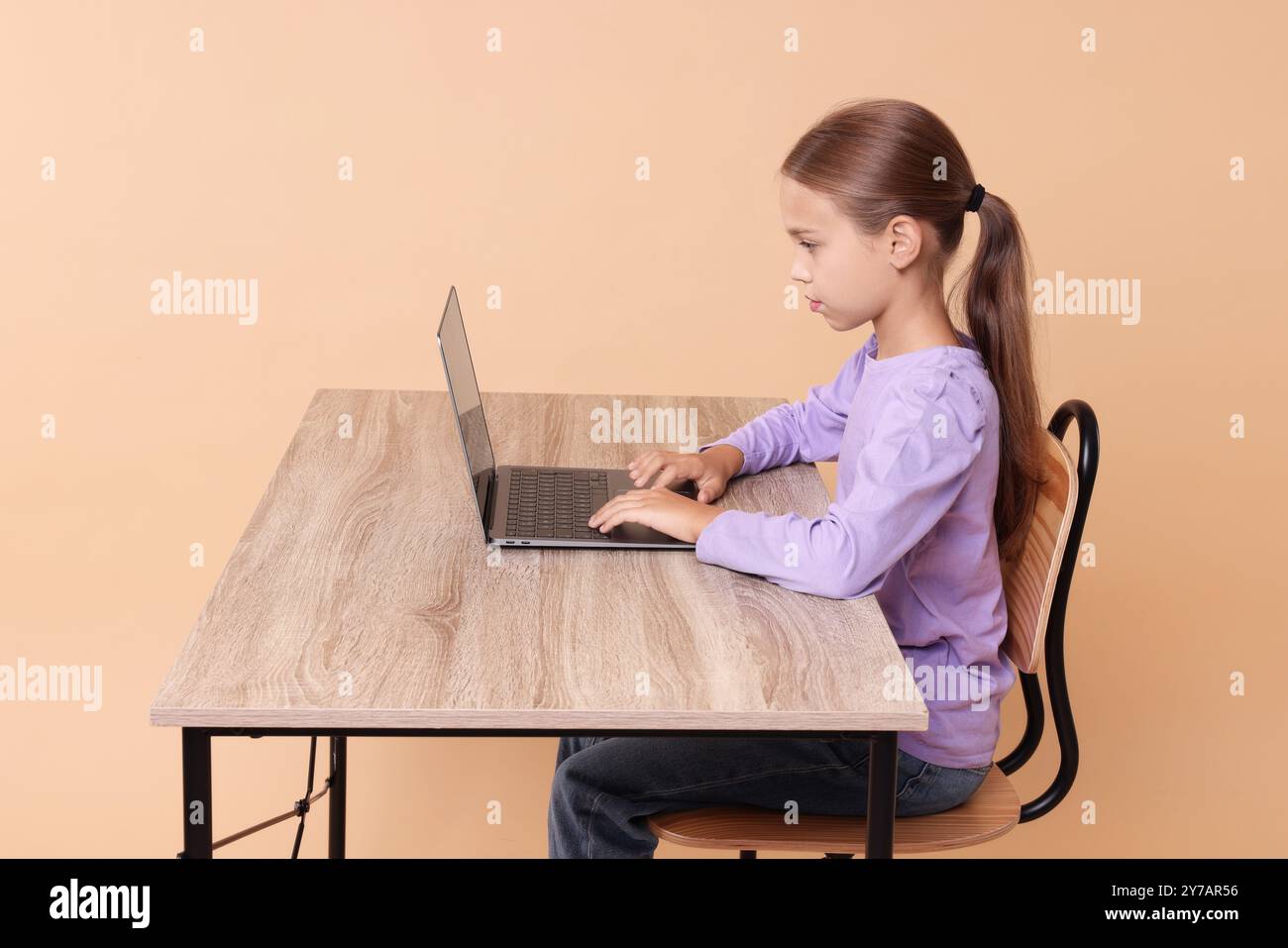 Girl with correct posture using laptop at wooden desk on beige ...