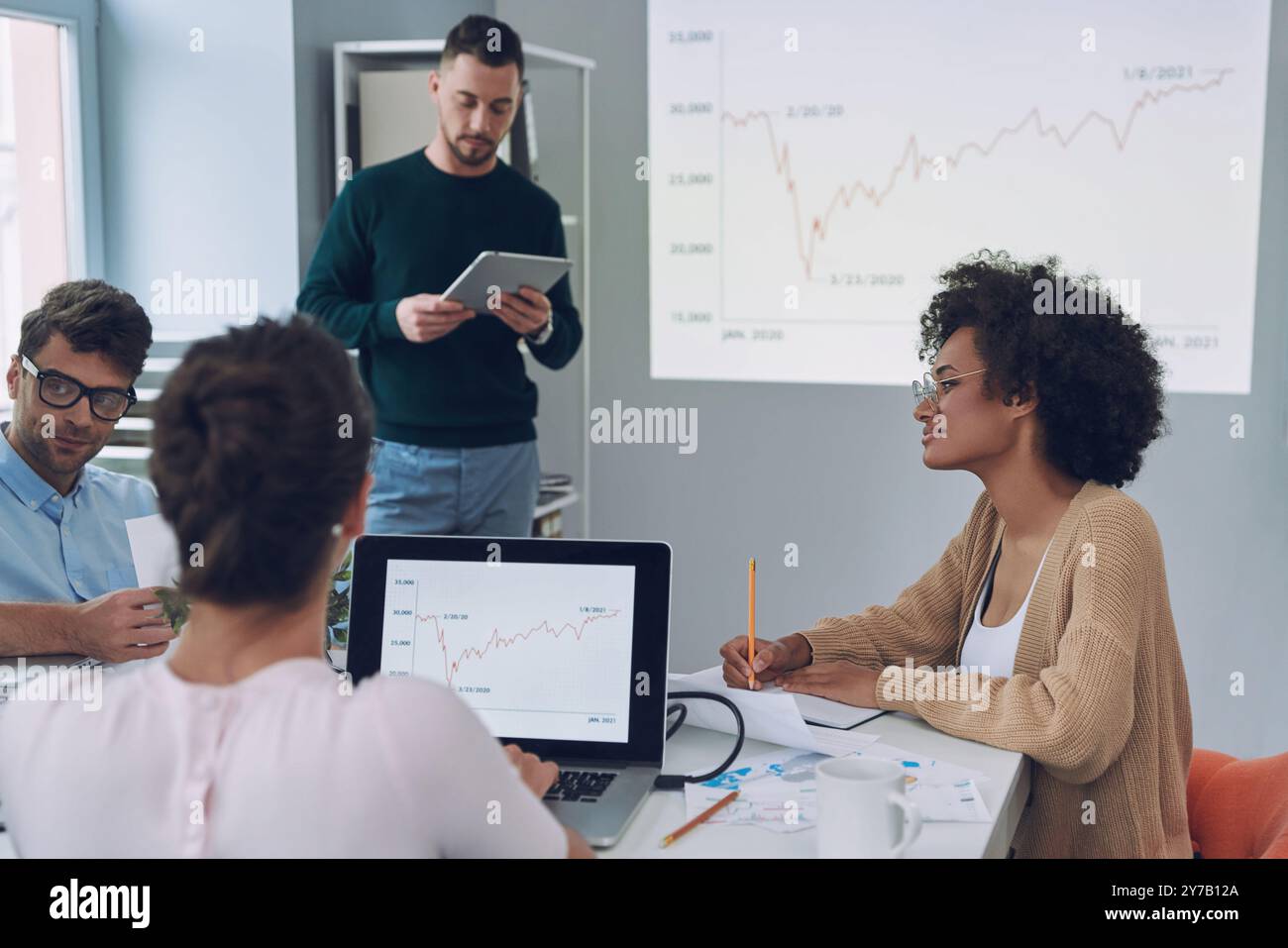 Group of young modern people in smart casual wear analyzing data on ...
