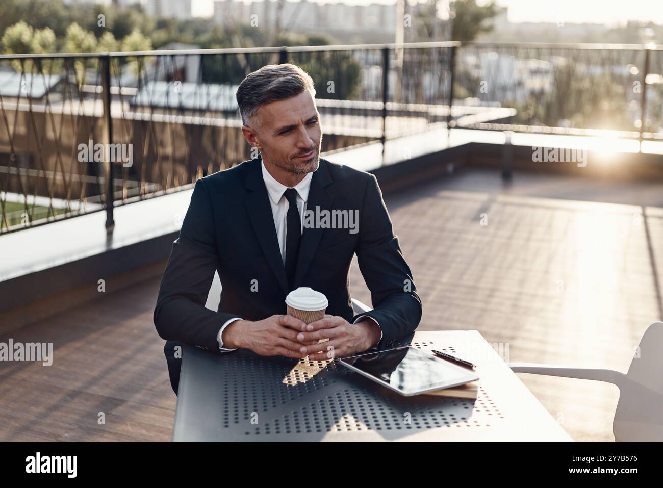 Confident mature man in formalwear enjoying coffee while sitting in cafe outdoors Stock Photo