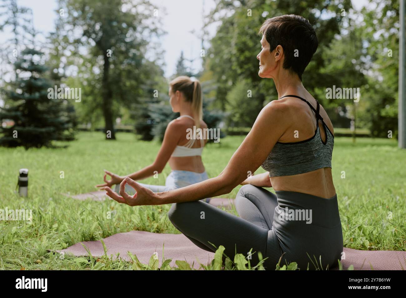 Unrecognizable women sitting on mat and focused on meditation in open air Stock Photo
