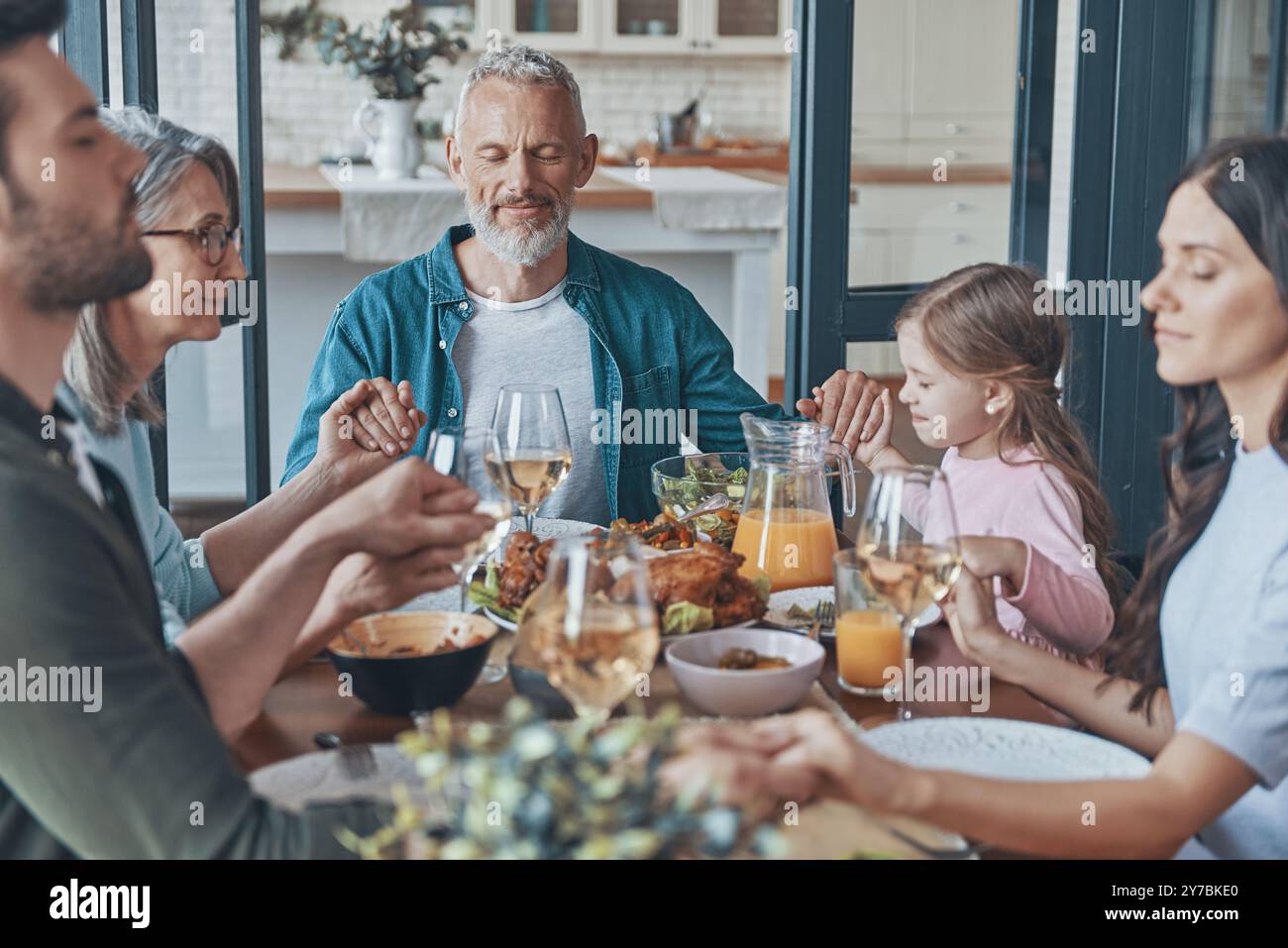 Happy multi-generation family holding hands and praying before having dinner Stock Photo