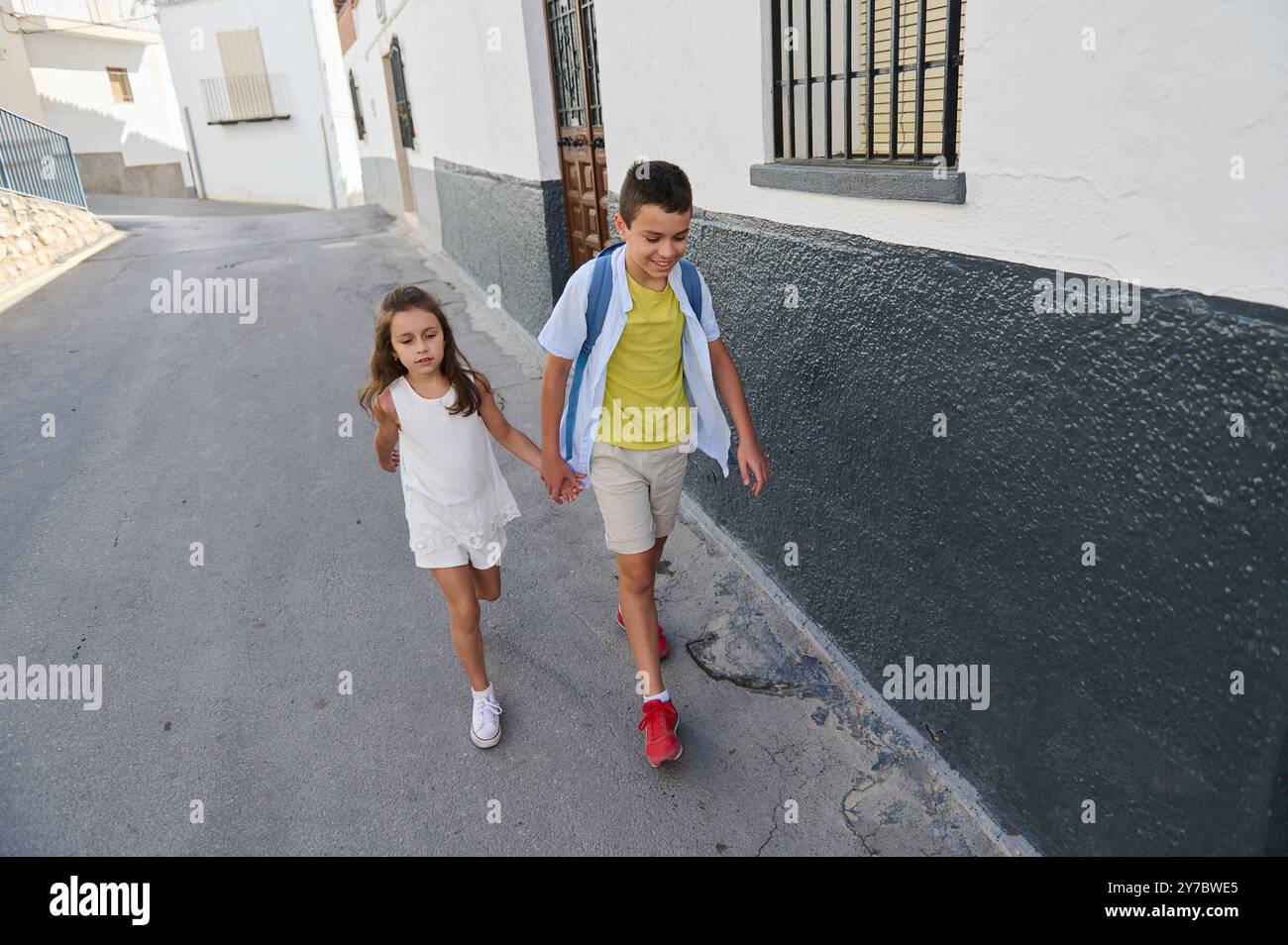 Brother and sister happily walking hand in hand along a peaceful urban ...