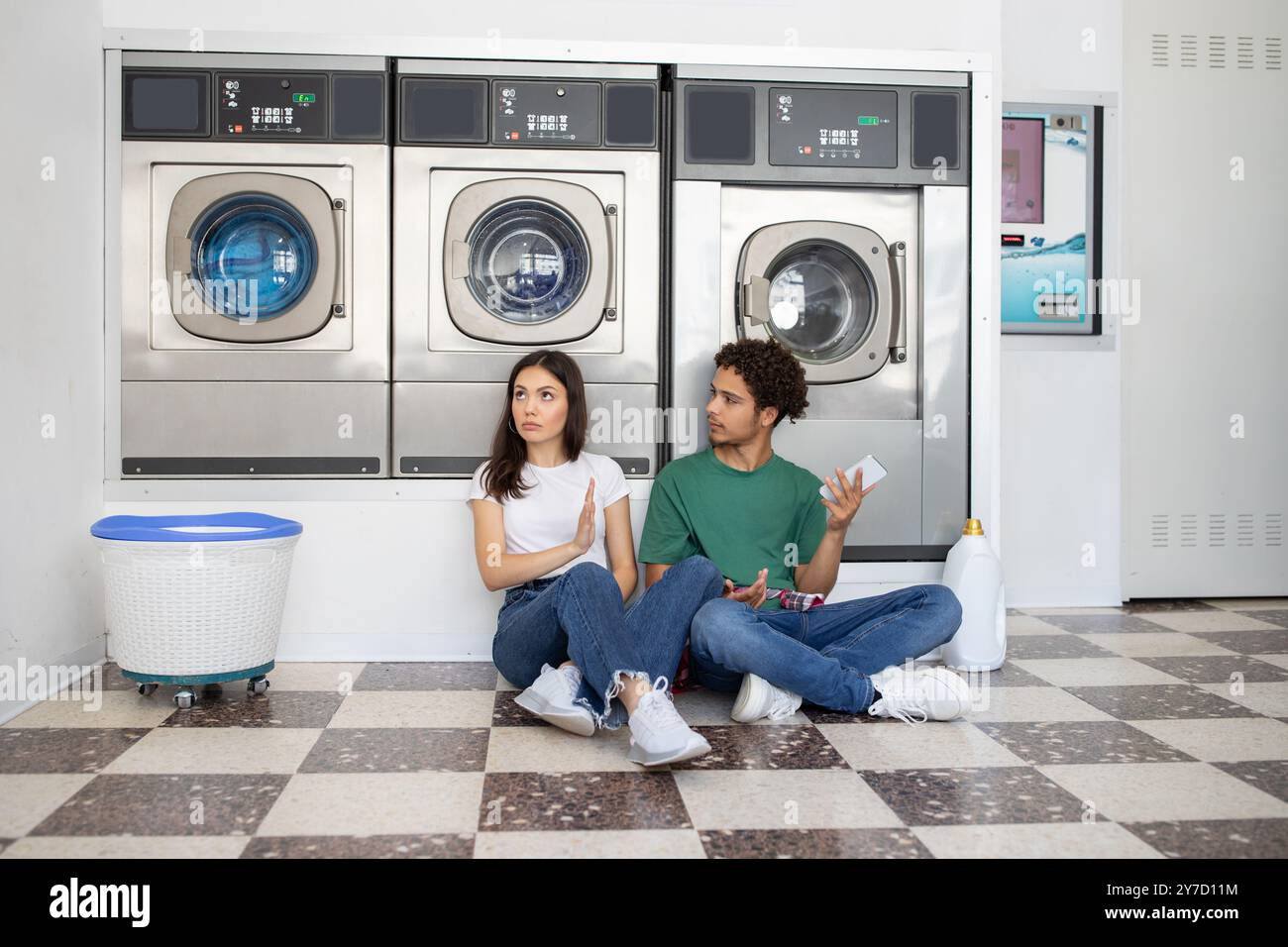Couple sitting on the floor of a laundromat while waiting for laundry ...