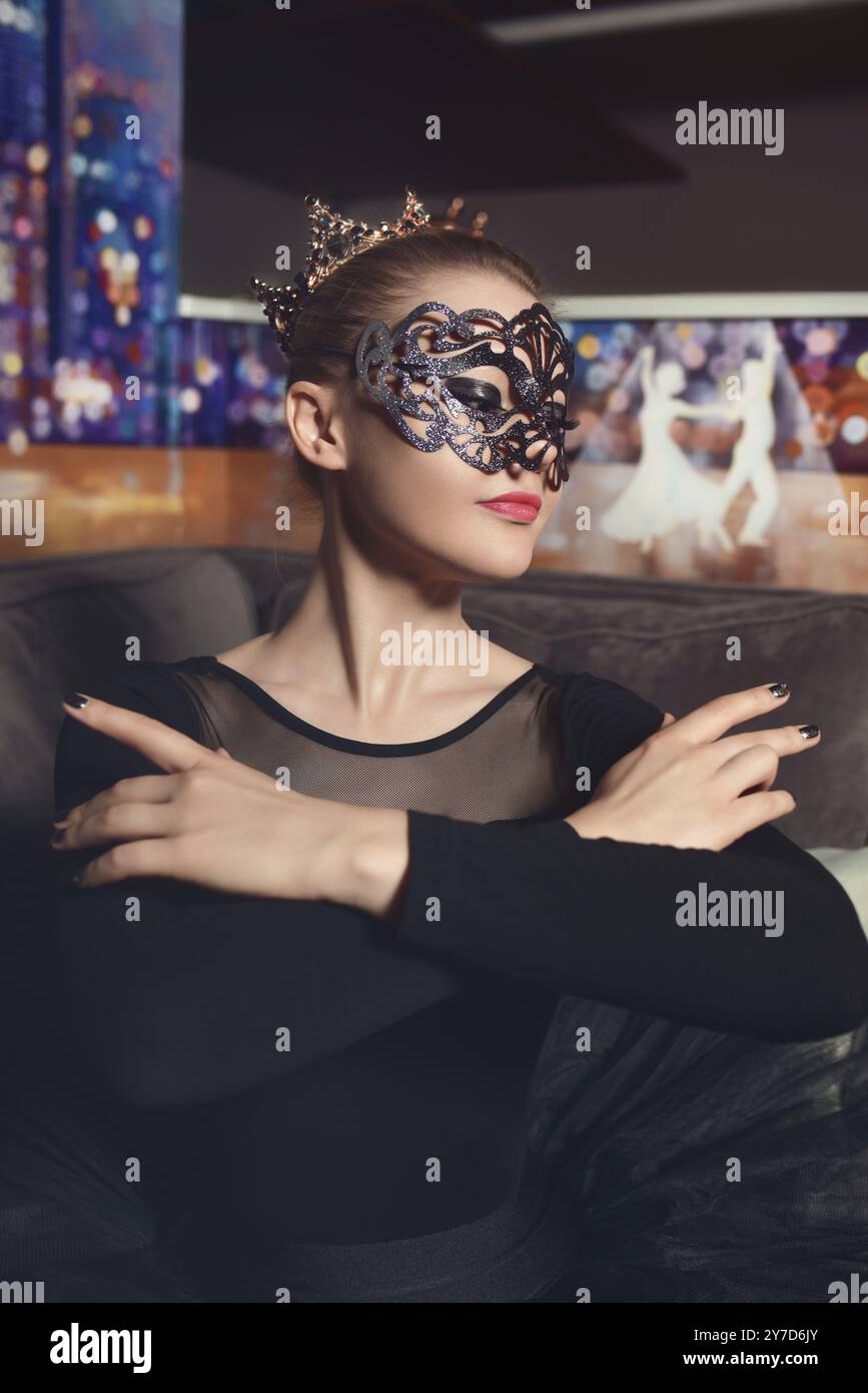 Portrait of a beautiful model ballerina wearing a crown and carnival mask in a black tutu in the studio. black swan ballerina Stock Photo