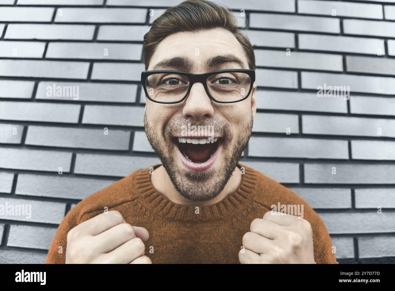 Young adult man over brown brick wall screaming proud and celebrating victory and success very excited, cheering emotion. Success concept Stock Photo