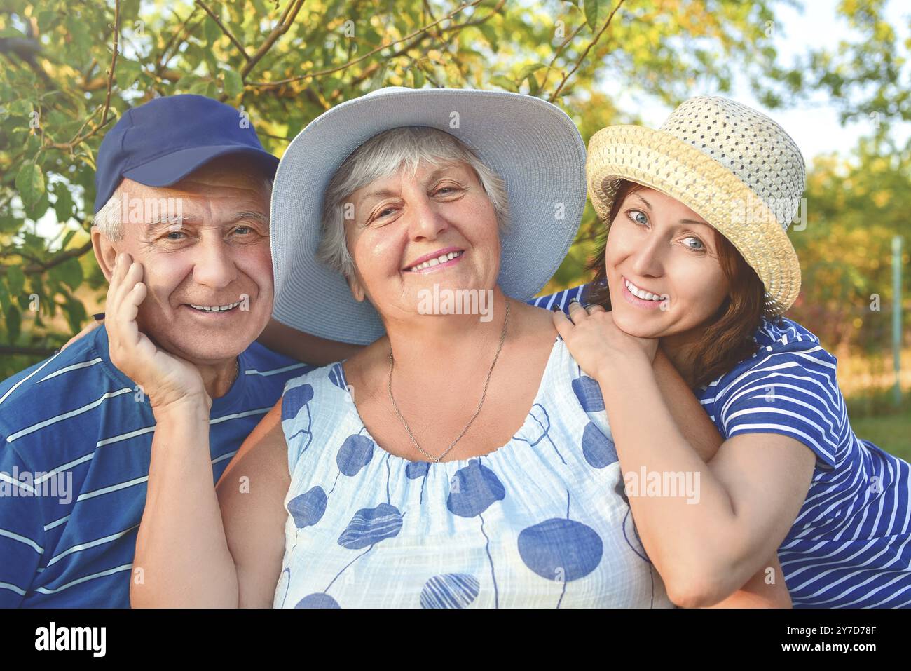 Beautiful senior couple is sitting on the bench in the park with their adult daughter. Grandma and grandpa are hugging and smiling. Real love and fami Stock Photo