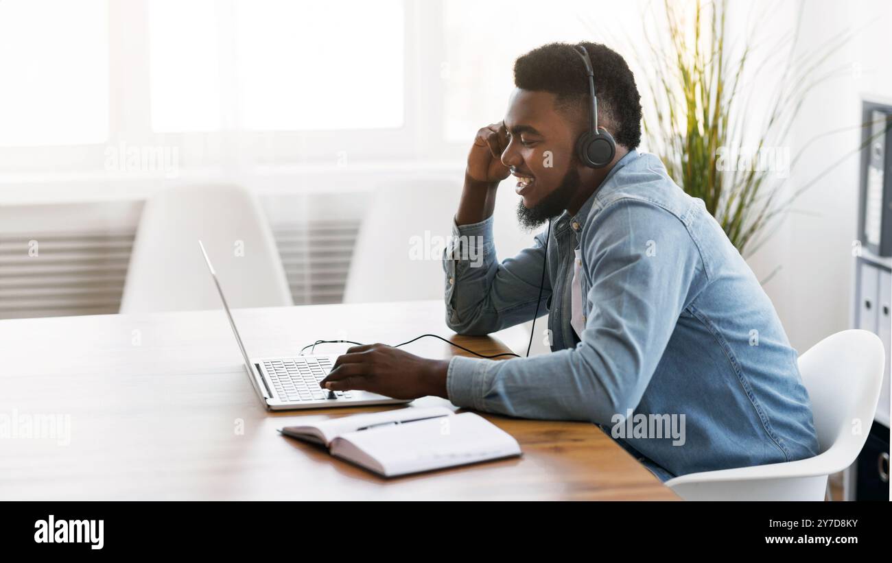 Cheerful manager wearing headset and using laptop, speaking with client Stock Photo