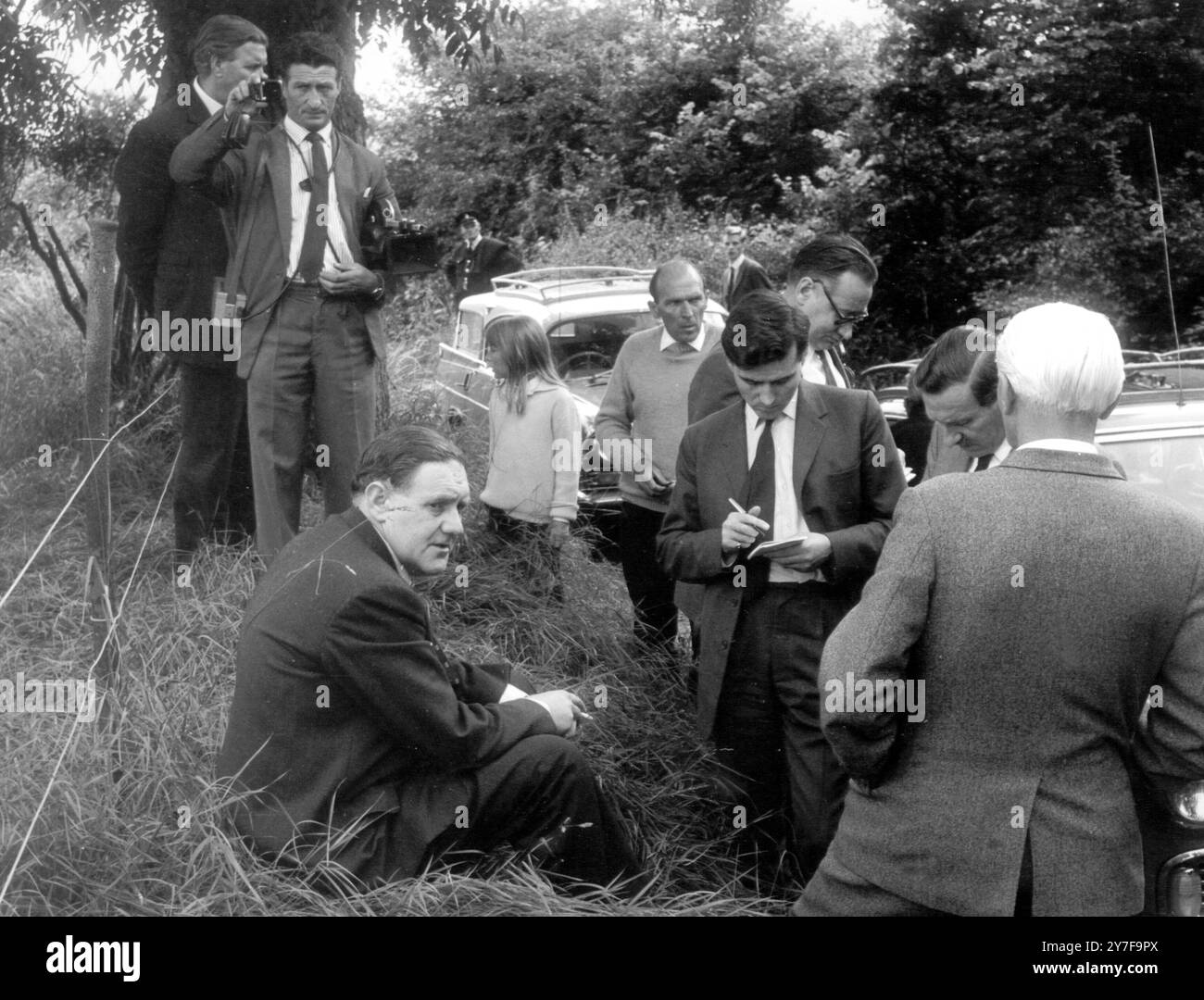 Cops Conference in the Countryside Detective Superintendent McArthur of Scotland Yard, sits in the long grass beside a farm track to give a press conference, after police followed a tip which led them to the farm hideout of the gang concerned in the 'Great Mail Robbery' - when £2 1/2 million was stolen from a train last week.  Oakley, Buckinghamshire, 14th August 1963 Stock Photo