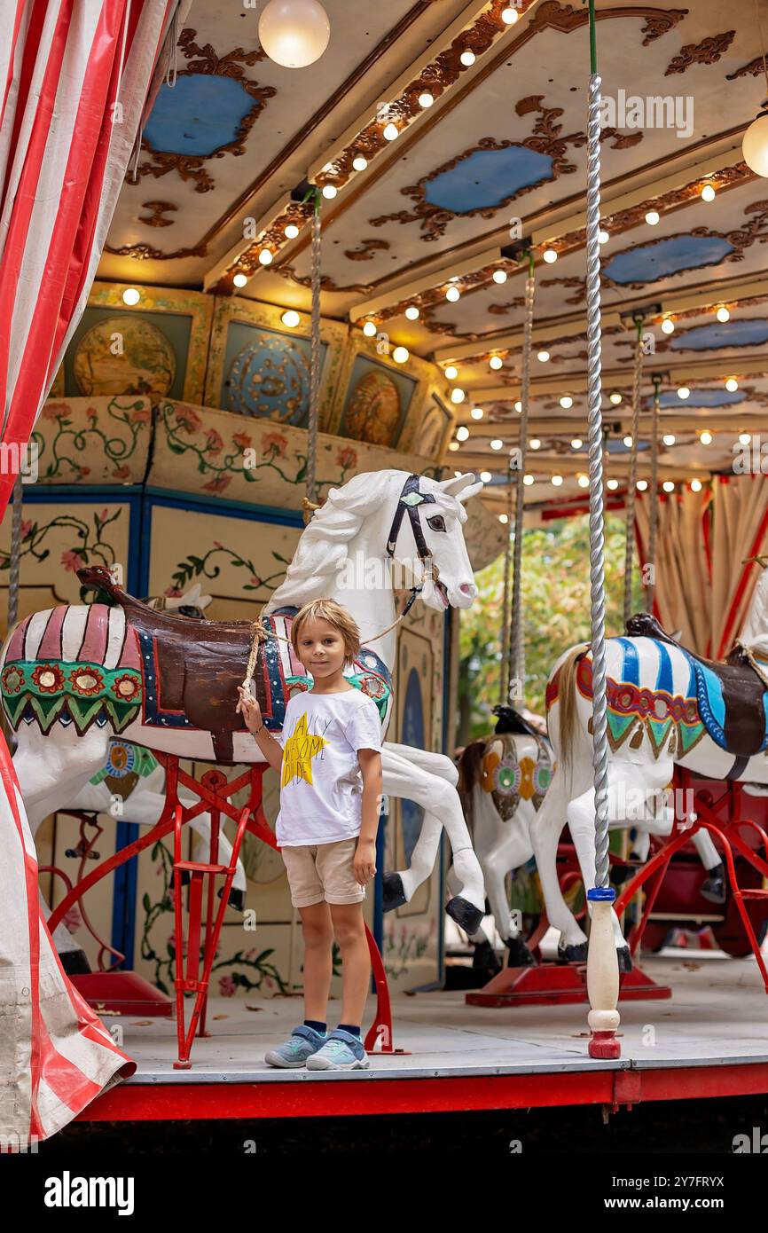 Cute blond child, going on Merry Go Round, kid play on carousel park ...