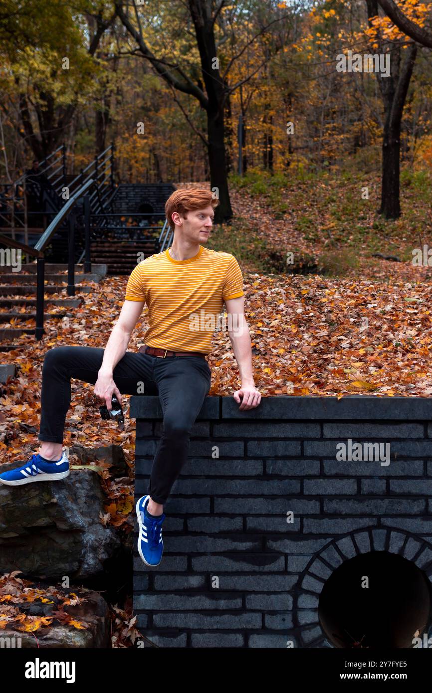 A young man in a yellow shirt relaxes on a stone wall Stock Photo