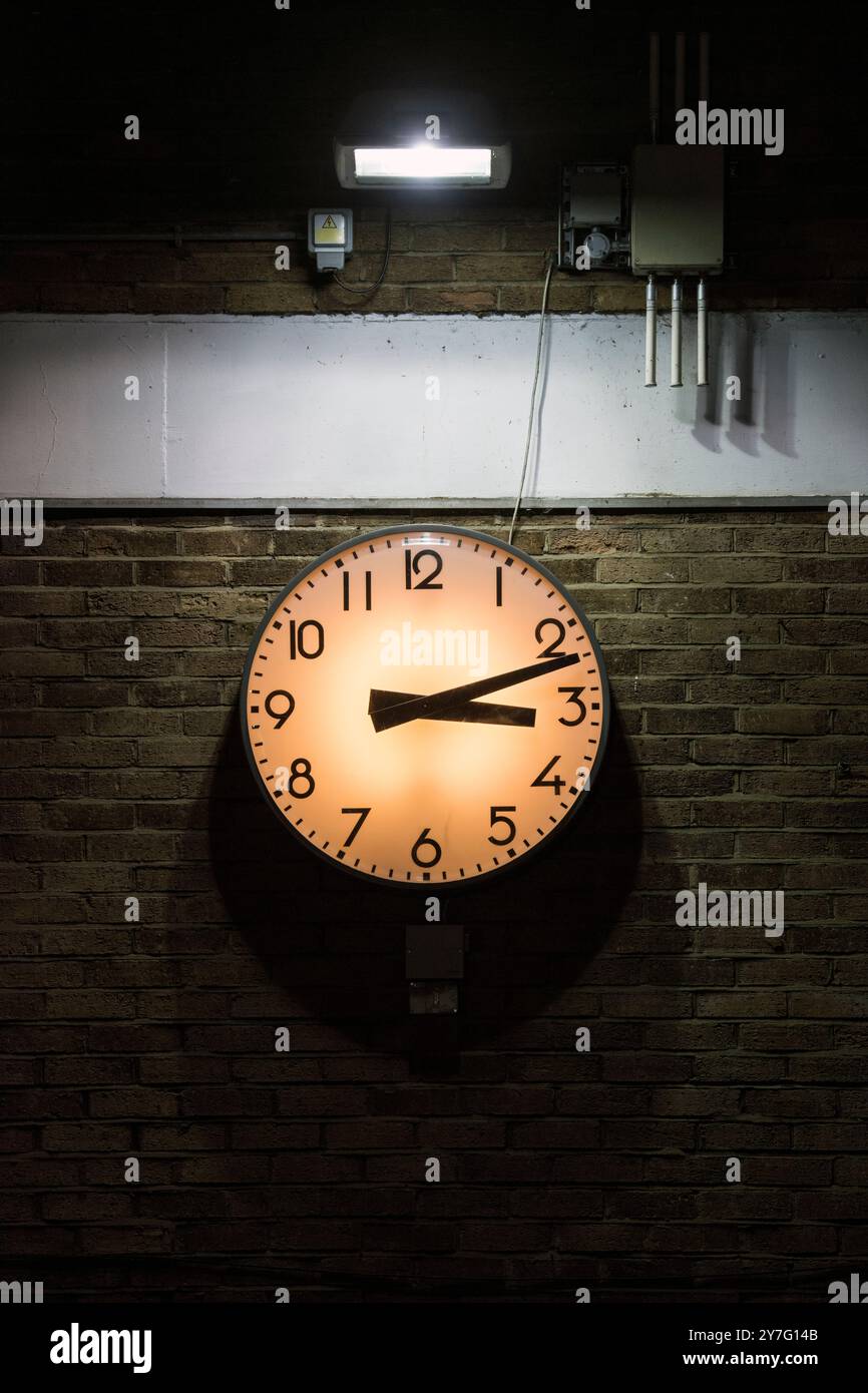 Wall-mounted clock in dimly lit industrial setting Stock Photo - Alamy