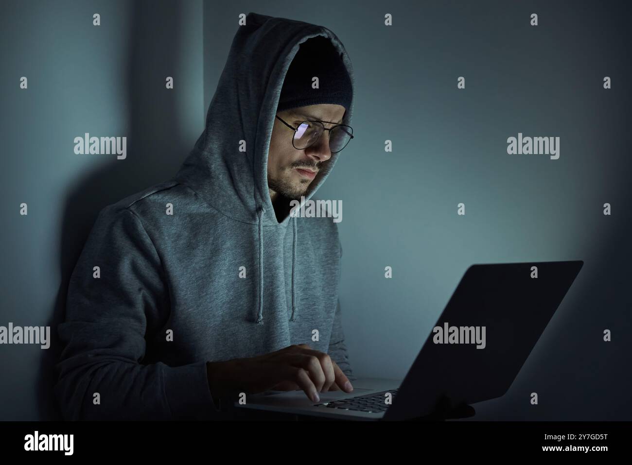 Confident young man in hooded shirt using computer while working late Stock Photo