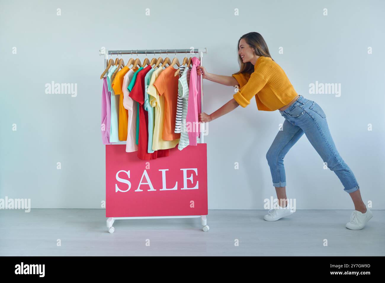 Cheerful young woman pulling a rack with colorful clothes Stock Photo ...