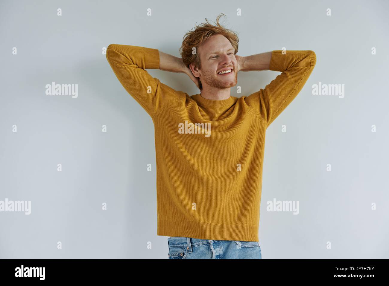 Relaxed young redhead man holding hands behind head while standing against wall Stock Photo