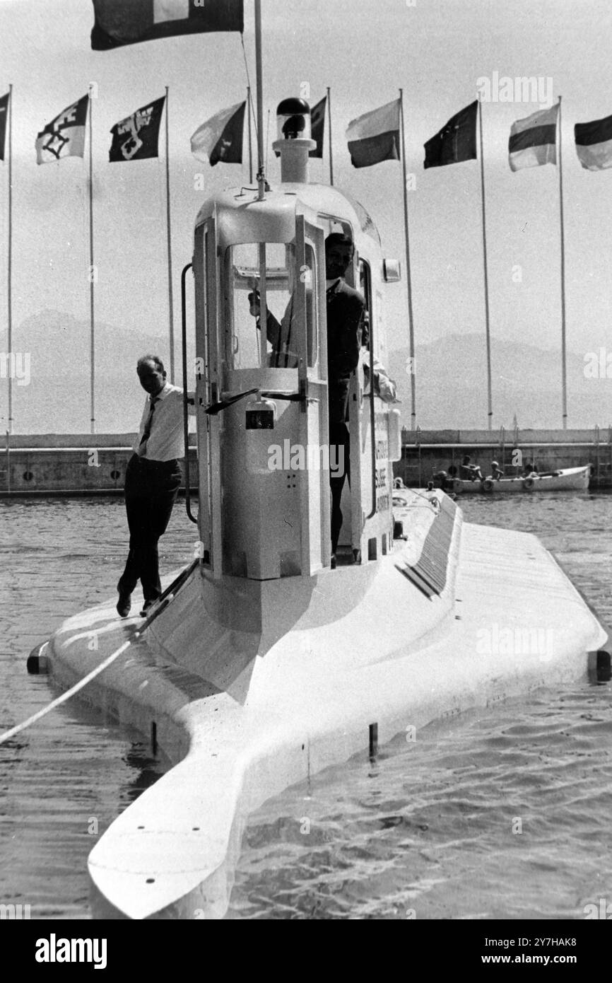 With engineer Spinnler standing on the hull, and Commander Arnould in the control tower, the world's first passenger carrying submarine, Professor Jacques Piccard's revolutionary ' Mesoscaph ' is seen at Vidy, Lausanne, Switzerland, after undergoing final driving trials supervised by a technical team selected by directors of the Swiss National Exhibition at Lausanne. The trials were carried out after the craft had undergone extensive modifications in which designer Professor Jacques Piccard did not participate by reason of dissension with the Exhibition directors. The craft, which can carry 42 Stock Photo