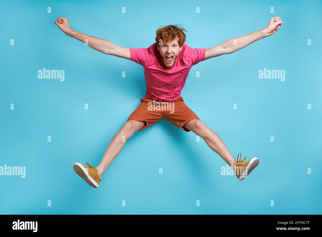 Cheerful young redhead man jumping against blue background Stock Photo