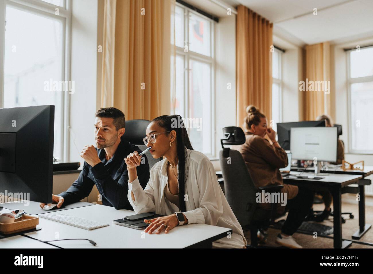 Female and male business professionals sharing computer screen while working in office Stock Photo