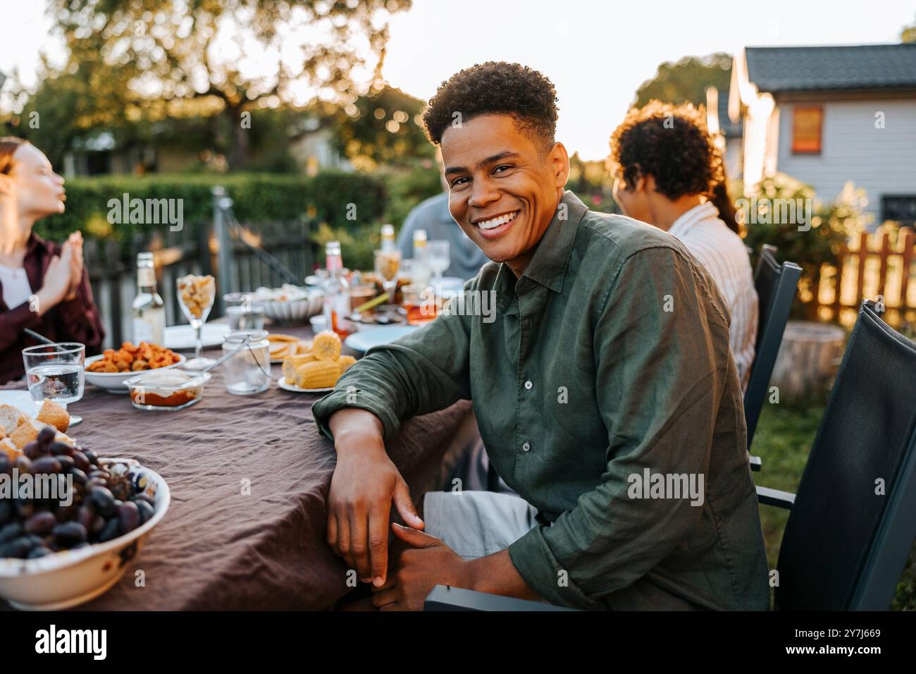 Portrait of happy curly hair young man sitting near dining table in back yard at dinner party Stock Photo