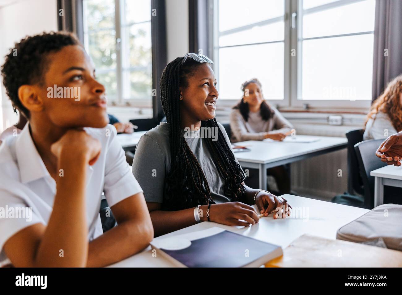 Happy teenage girl sitting beside male classmate near desk in classroom at junior high school Stock Photo