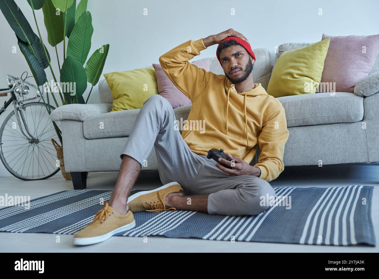 Frustrated young African man carrying joystick while sitting on the floor at home Stock Photo