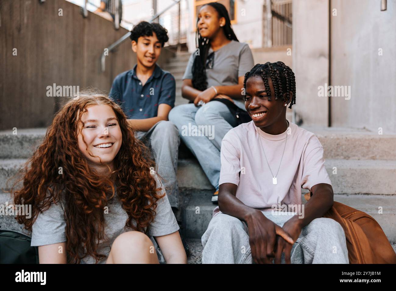 Happy teenage boy sitting with friends on stairs of junior high school Stock Photo