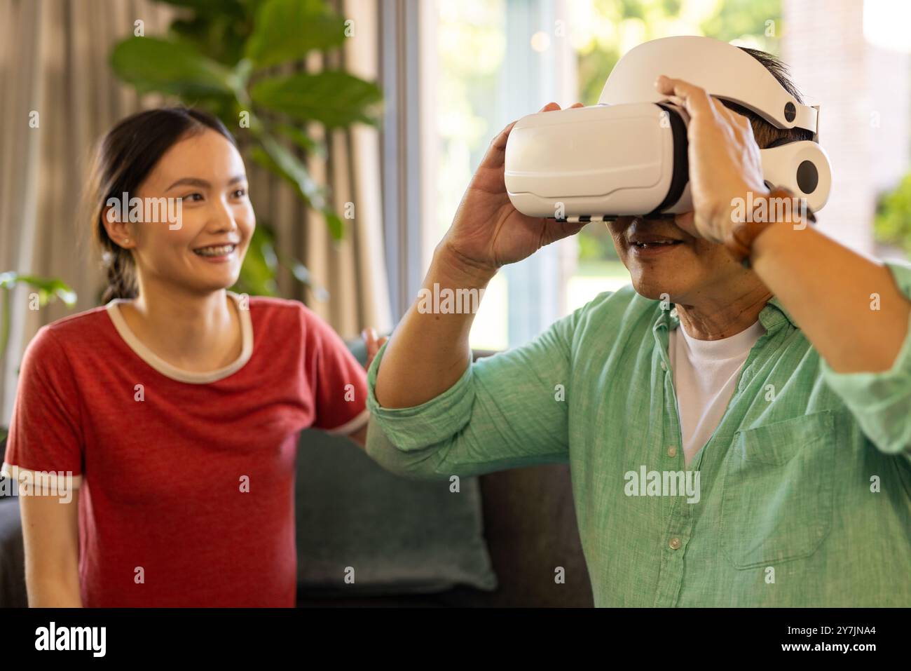Using VR headset, father exploring virtual reality while daughter smiling nearby Stock Photo