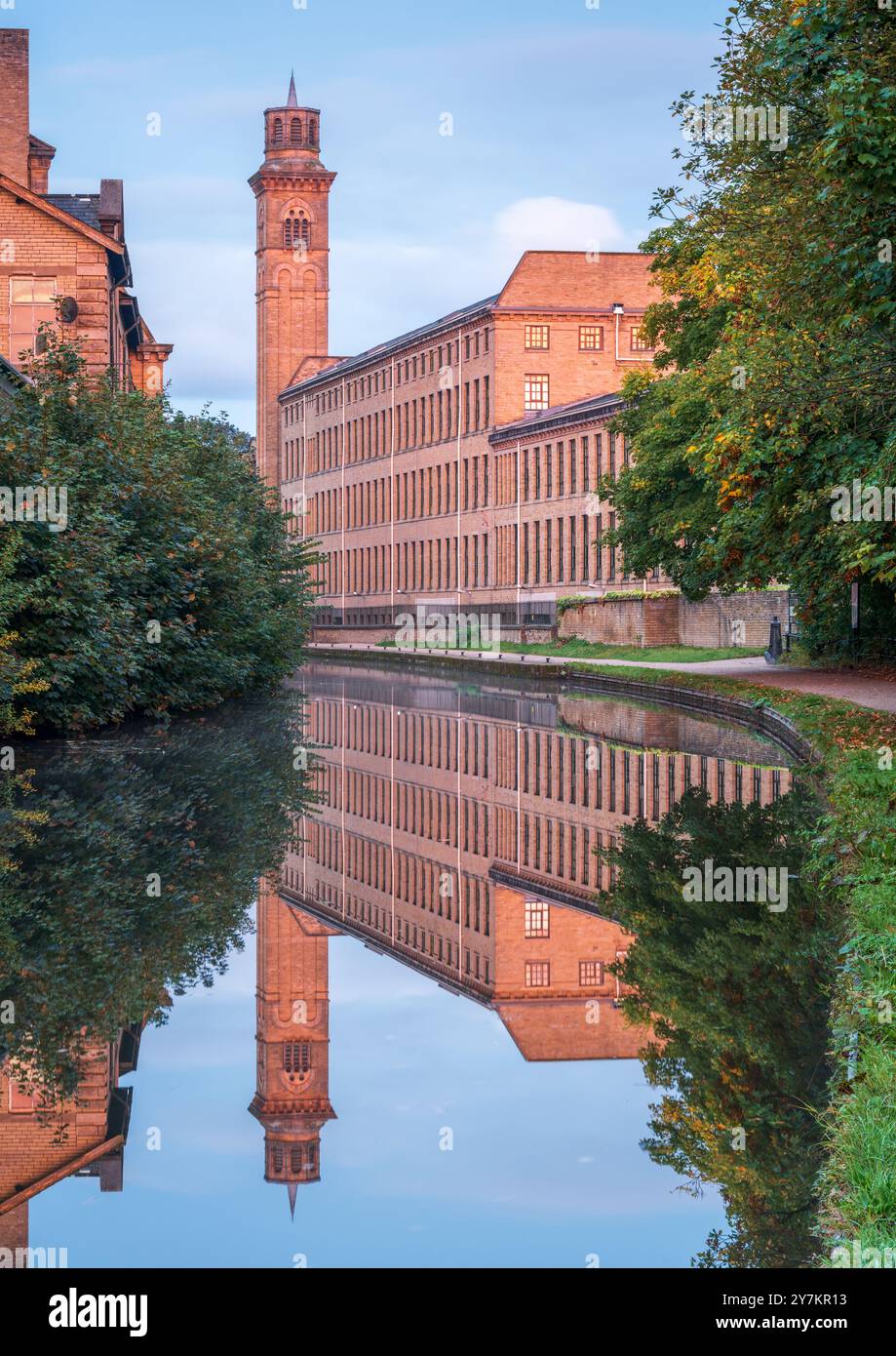 The New Mill building at Salts Mill, Saltaire, glows a deep orange on a calm September morning in the reflected light of a vivid Yorkshire sunrise. Stock Photo