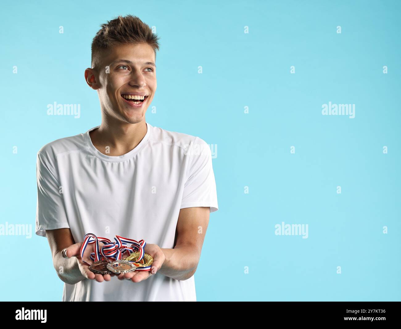 Happy winner with different medals on light blue background. Space for ...