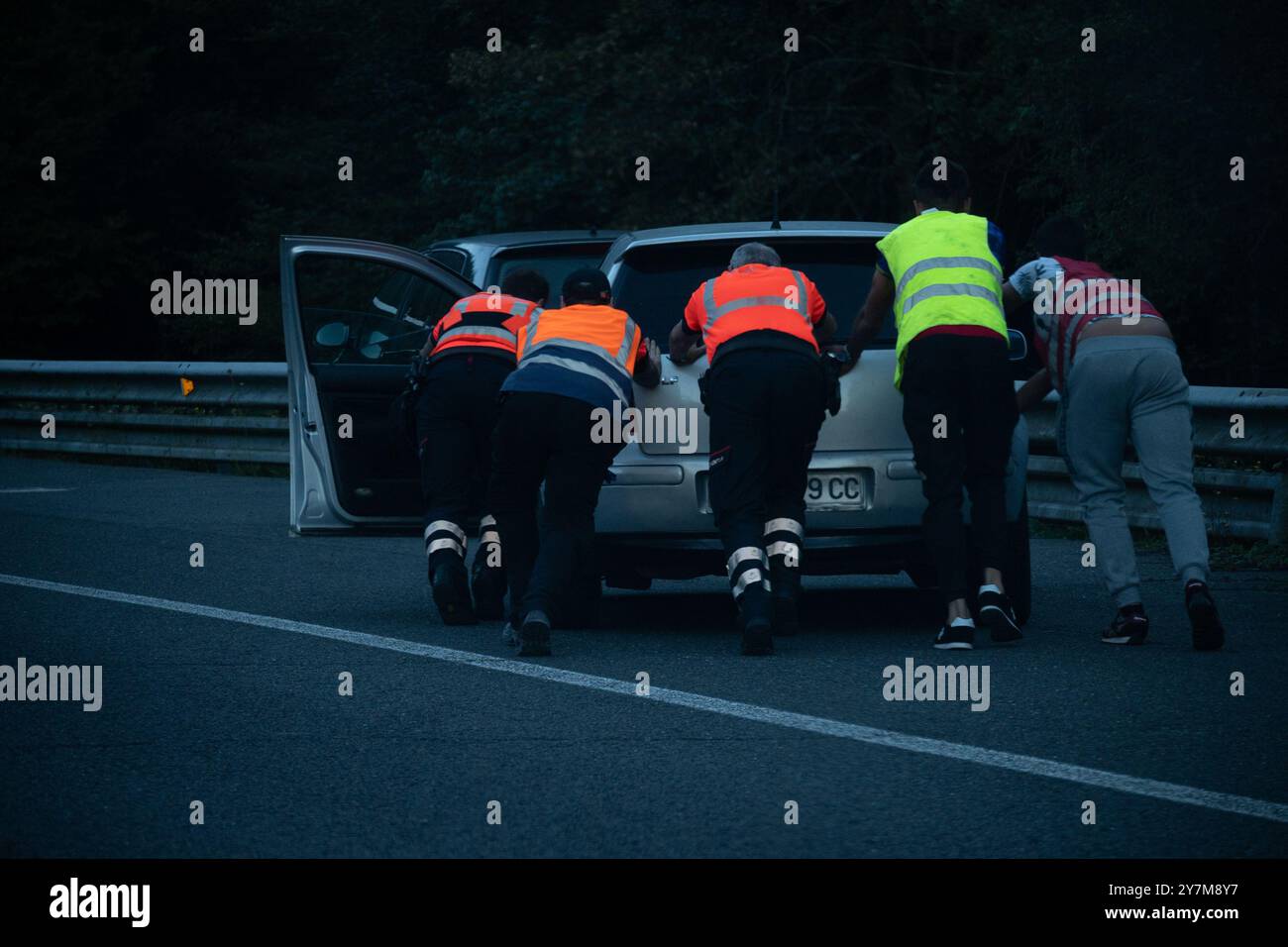 Group of people in safety vest pushing a broken car in road Stock Photo